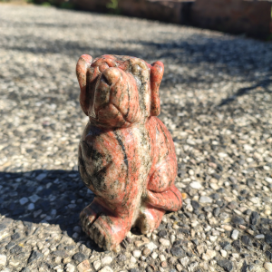 Unakite dog carving with natural green and pink tones, displayed on a rock outdoors.
