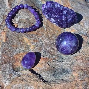 Amethyst crystal bundle with multiple natural purple amethyst pieces arranged together on a rock outdoors.