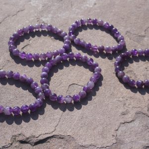 Amethyst bracelet with natural purple beads resting on a rock outdoors.