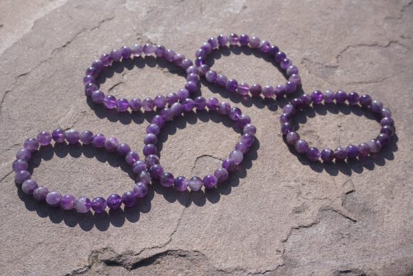 2026/08/1000006073.jpg Amethyst bracelet with natural purple beads resting on a rock outdoors.