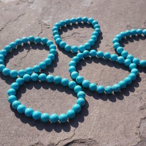 Turquoise bracelet with blue-green beads resting on a natural rock outdoors.
