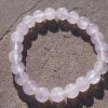 2026/08/1000006107.jpg Rose Quartz stretch bracelet with soft pink beads and natural variations resting on a rock outdoors