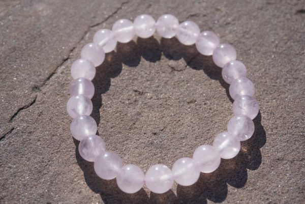 2026/08/1000006107.jpg Rose Quartz stretch bracelet with soft pink beads and natural variations resting on a rock outdoors