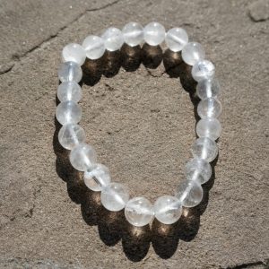 Clear Quartz stretch bracelet with transparent beads and natural inclusions resting on a rock outdoors.