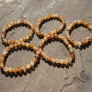 "A close-up of 5 stretch bracelet made from round, polished golden-yellow citrine crystal beads resting on a Rock